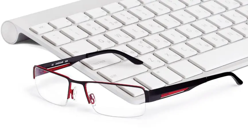 Detailaufnahme einer schwarz-roten Brille vor einem Laptop mit Tastatur im Hintergrund