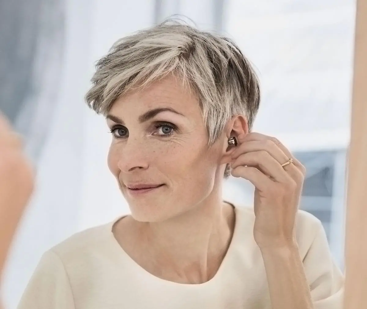 Frau setzt sich ein Hörgerät ins Ohr